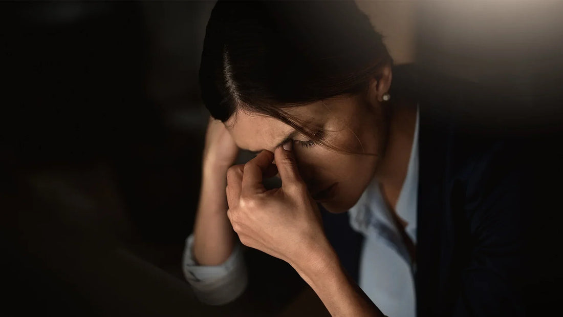 Stressed woman holding her forehead in low light, representing anxiety and mental fatigue, highlighting the stress-relief benefits of KSM-66 Ashwagandha.