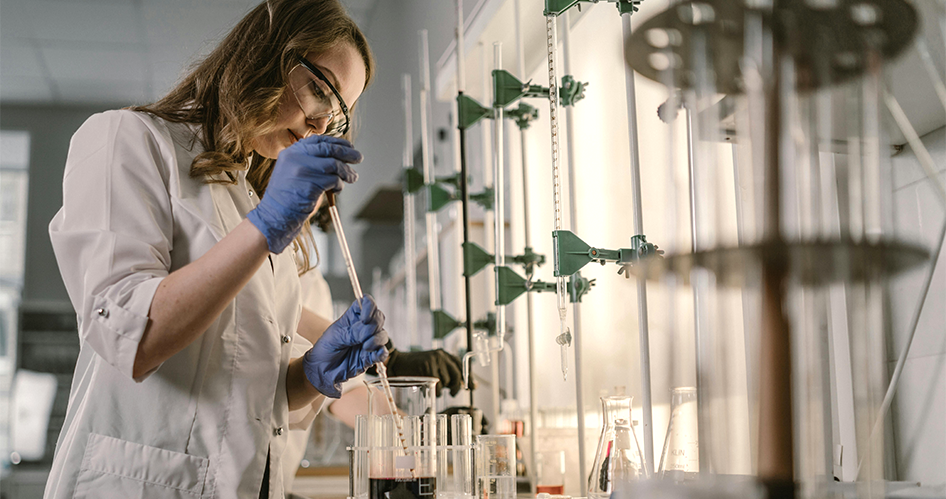 Lady in a lab coat and gloves conducting an experiment with laboratory equipment.