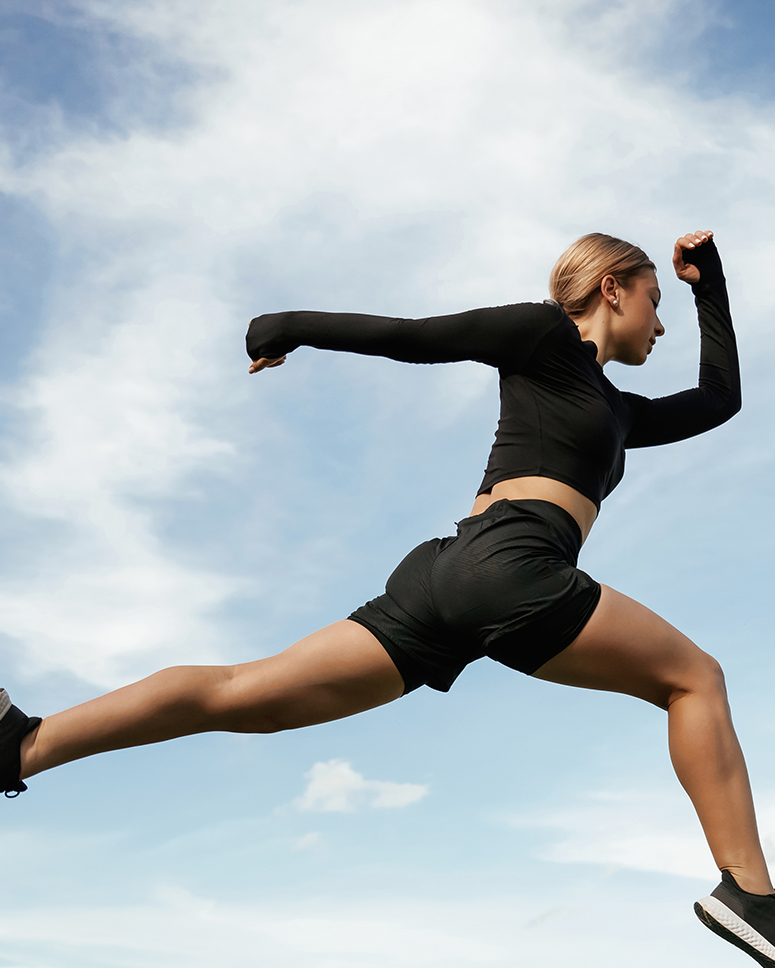 Woman athlete jumping outdoors under blue sky with bold “Your Fitness, Our Priority!” text and Boost Energy call-to-action banner promoting active lifestyle and wellness.